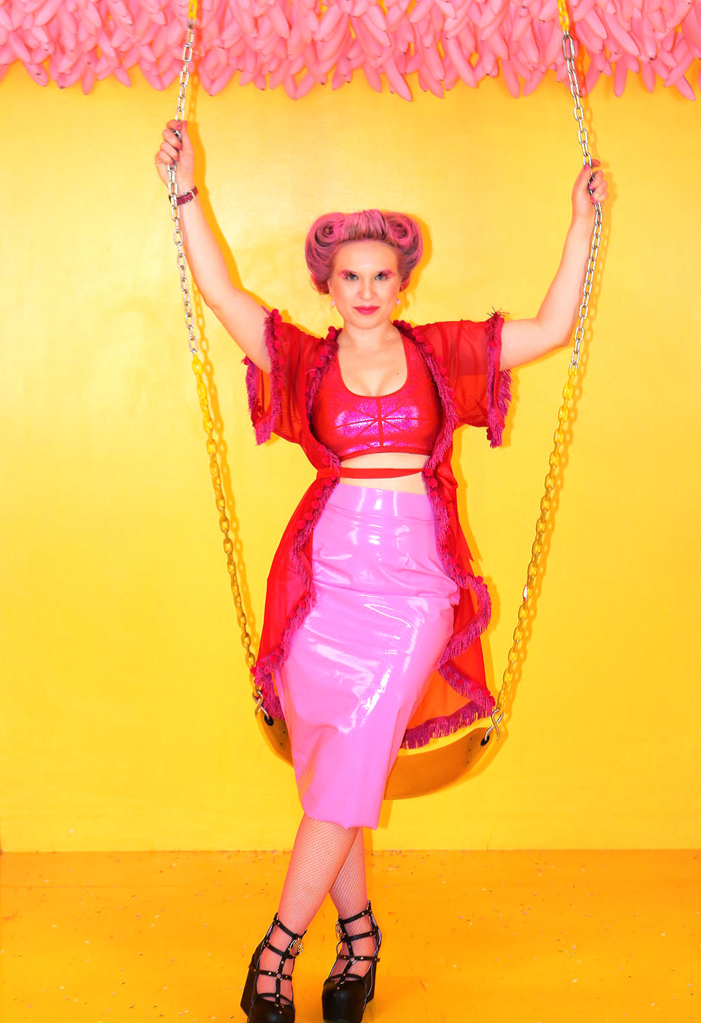 model in a swing wearing a wet look high glossy pink latex knee long skirt