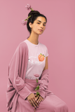 model wearing blush girly slim fitted t-shirt with short sleeves with a print in a front of a whip hitting a peach and the white text kinky 