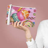 person holding clutch made of vegan leather with candy print on pink background. Golden metal zipper and white loop handle